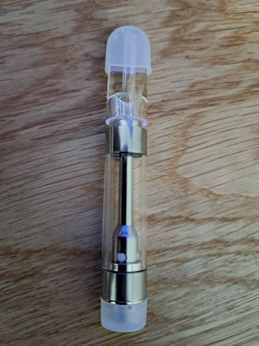 A glass vaporizer with a V10-SS - PCTG Flat Tip -1ml sitting on top of a wooden table.